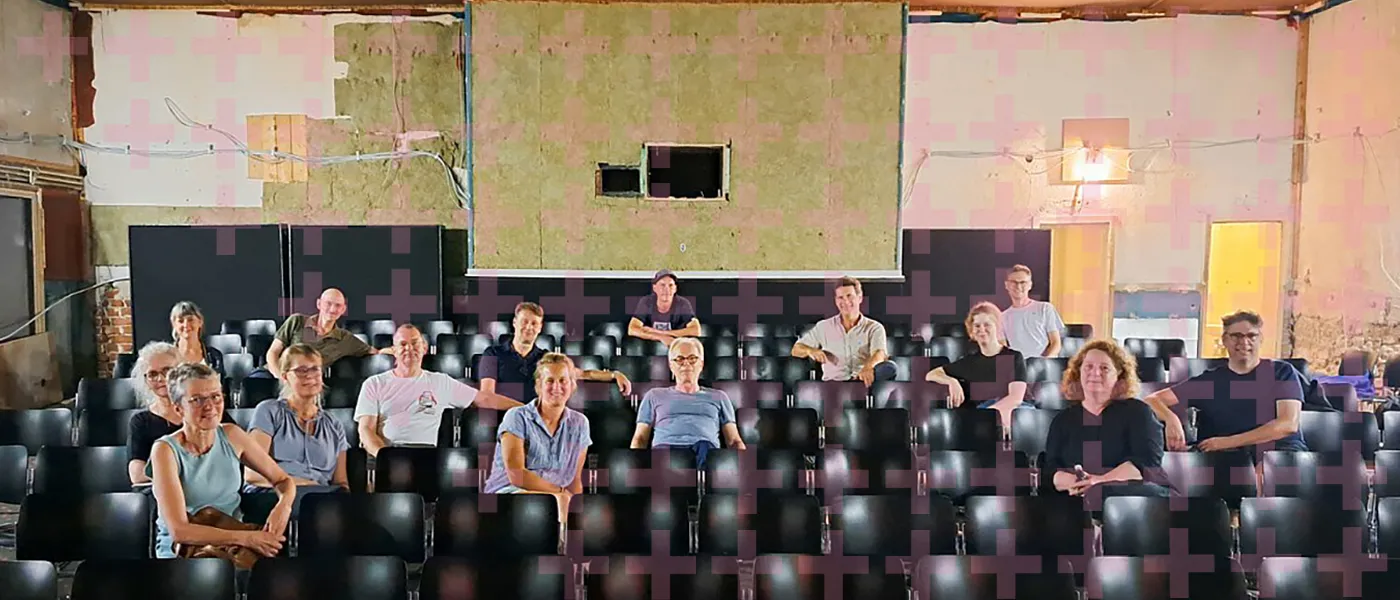 Mitglieder des Kino und Kultur Detmold e.V. posieren für ein Pressefoto im alten Kaiserhof Kinosaal - transparente Pluszeichen liegen als Pattern über dem Motiv